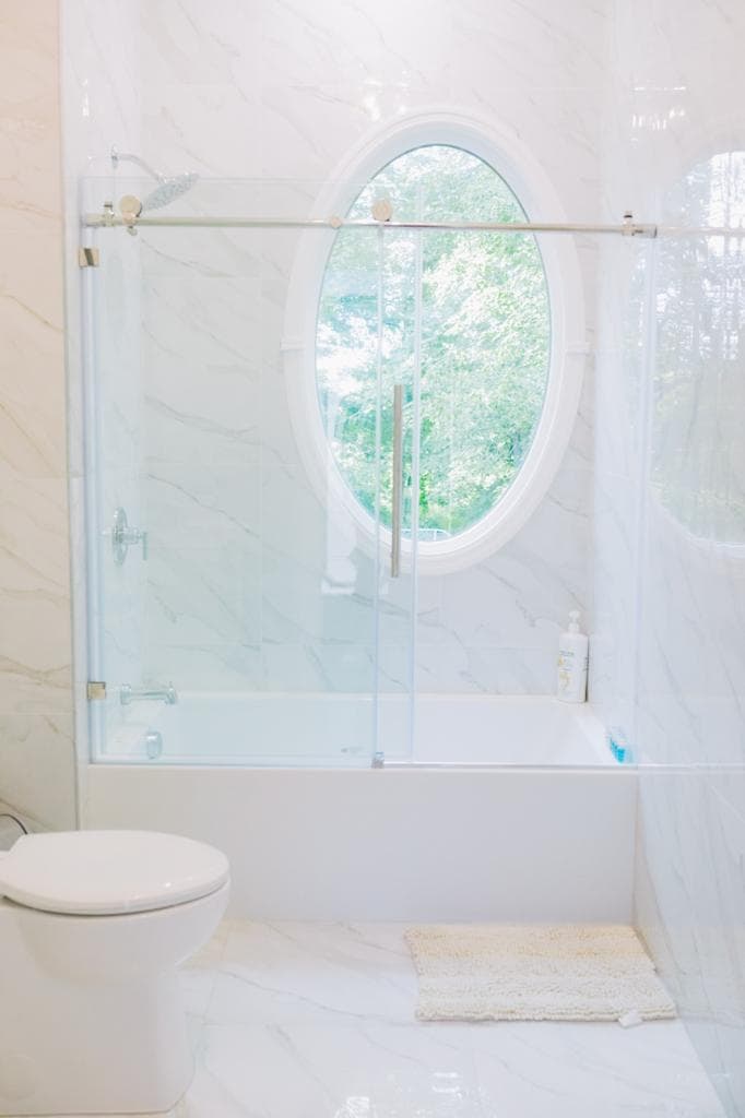 Marble bathroom with tub, glass shower, and oval window